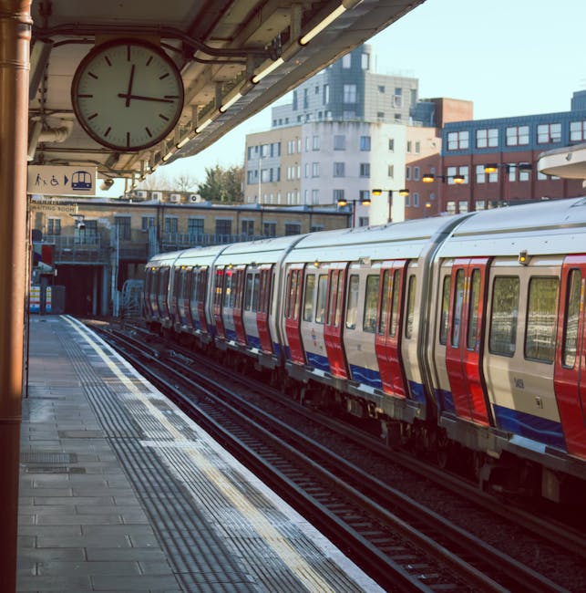 The image depicts a railway station platform at sunset, with the train tracks running into a tunnel illuminated by the warm glow of the setting sun. The platform surface features tactile paving strips